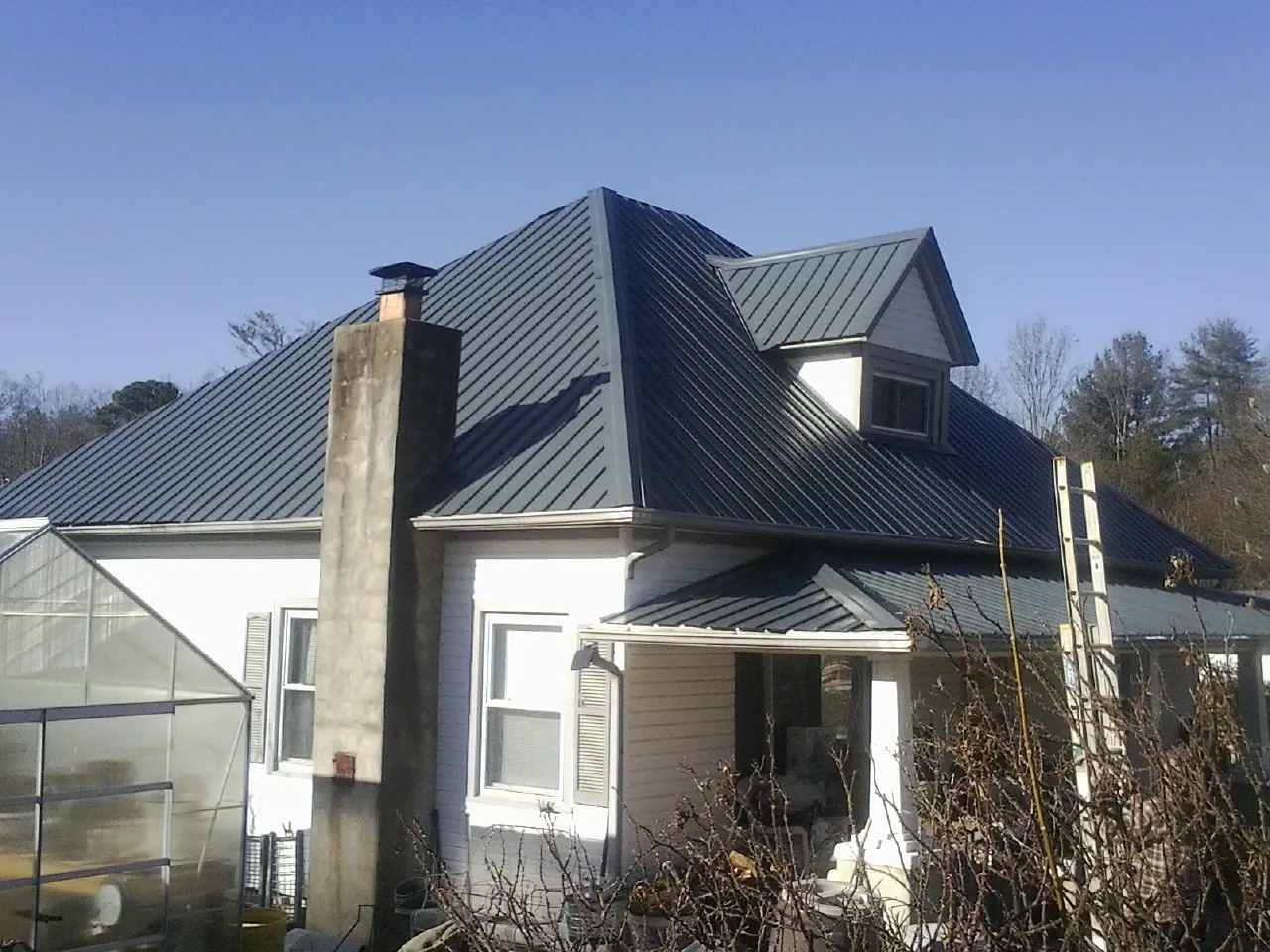 Dark blue standing seam metal roof on a white farmhouse with dormer — Slate & Tile Roof Repair by Roofing Brothers in Breesport