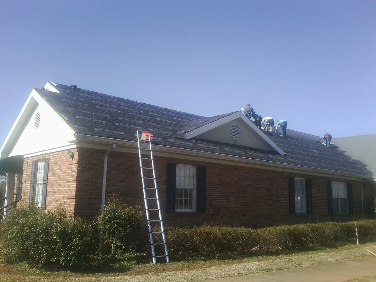 Crew tearing shingles off a brick ranch roof with a ladder set — Metal Roof Repair work by our crew in Breesport
