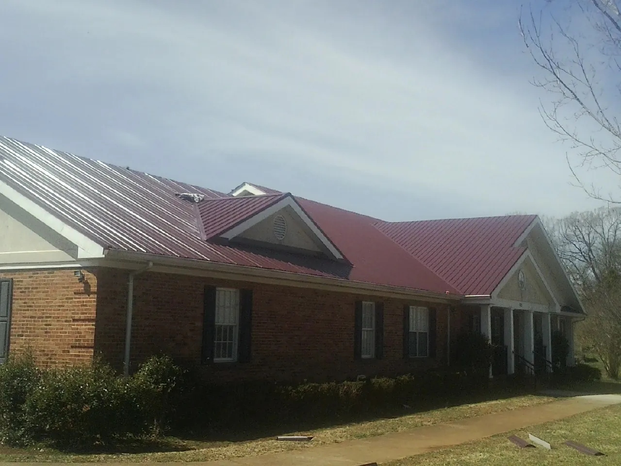 Red metal roof with gabled entries on a long brick building, from a Hail Damage Roof Repair job in Breesport