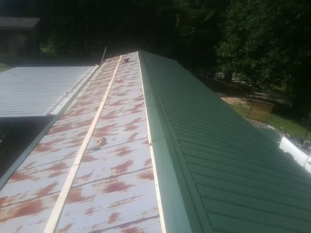 Old rusted panels beside newly installed green metal roofing — Wind Damage Roof Repair by Roofing Brothers in Breesport