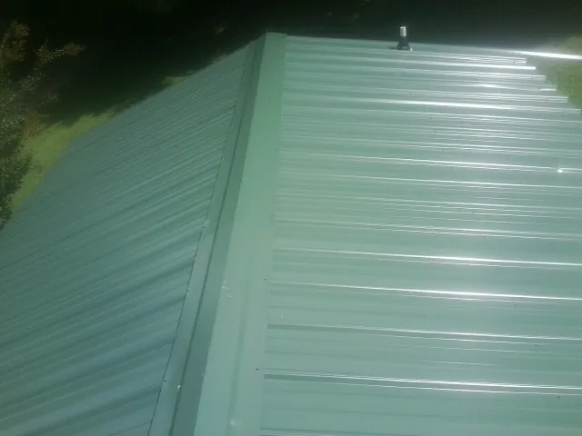 New green metal panels meeting at the ridge of a roof — Flat Roof Repair work by our crew in Breesport