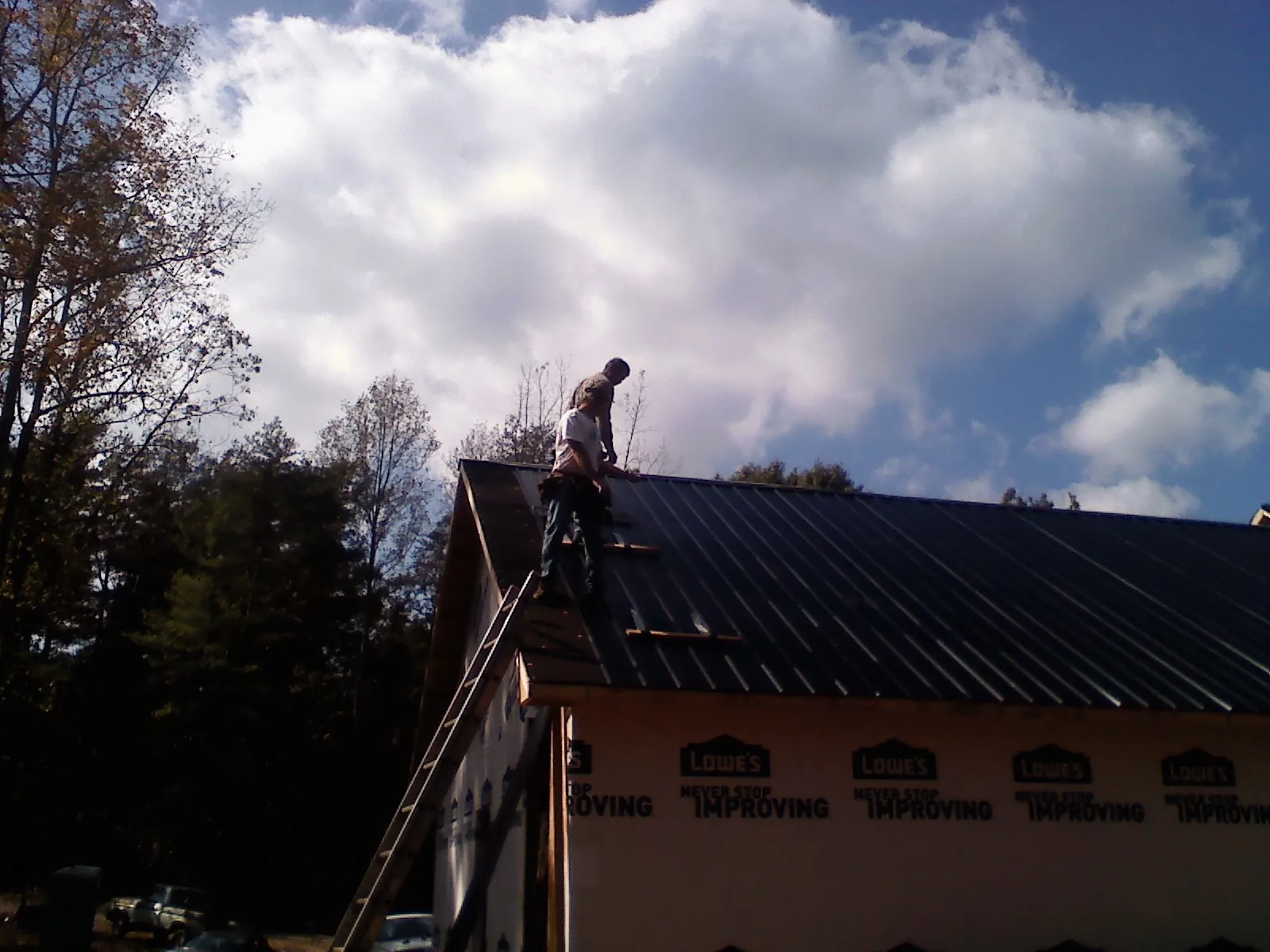 Roofer fastening dark metal panels high against a cloudy sky, from a Roof Inspection job in Breesport