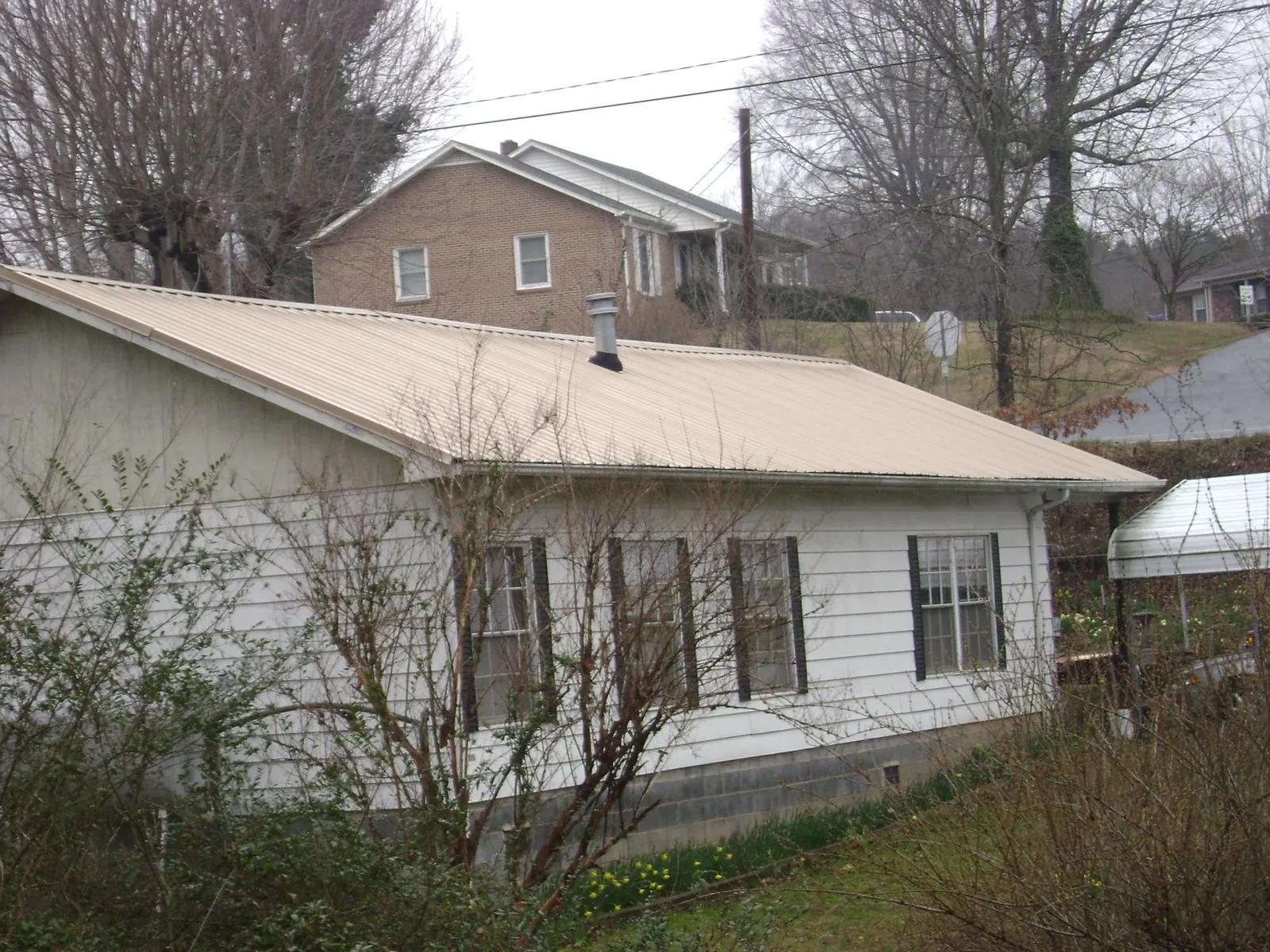 Tan metal roof on a white sided house set into a hillside — Commercial Roofing by Roofing Brothers in Breesport